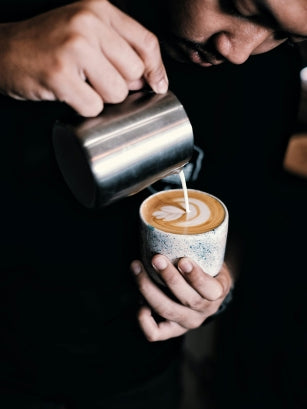 man pouring milk in a cup of coffee