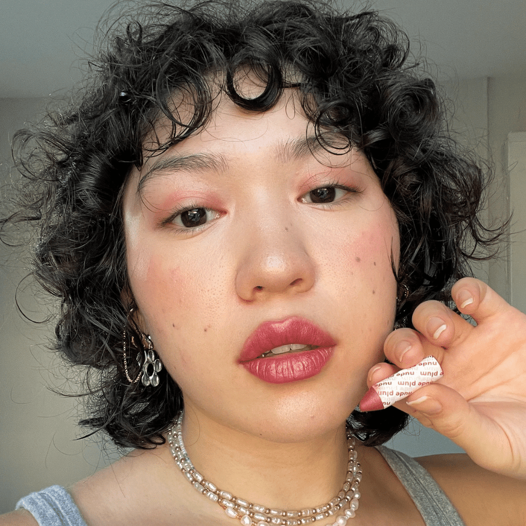 woman with light skin holding Nude Plum Lip-to-Lid Balmie against her face