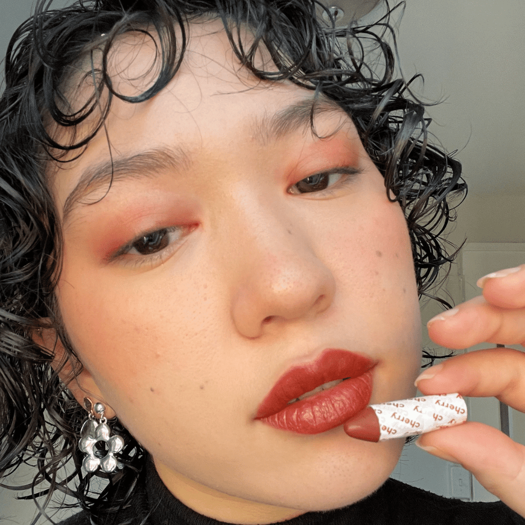 model holding Cherry Lip-to-Lid Balmie against face