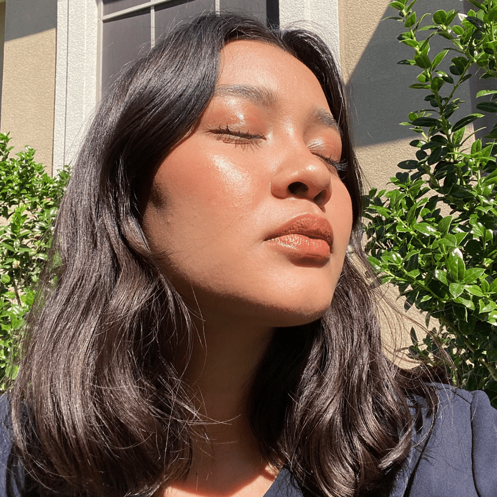 woman wearing Cinnamon + Champagne Lip-to-Lid Balmie facing the sun